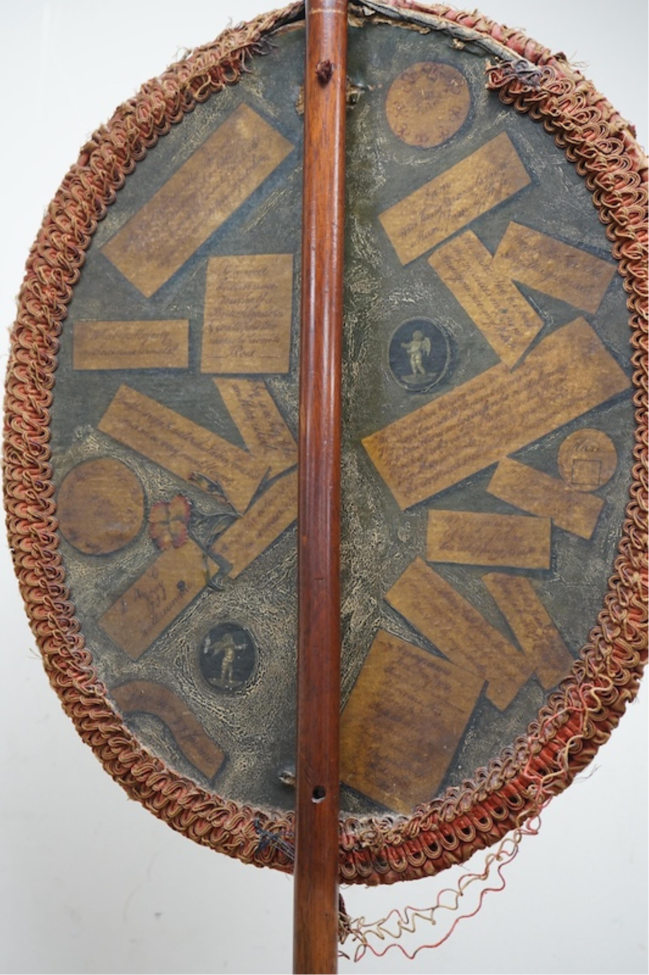 An oval Regency fire screen painting of a shepherd boy with his dog and a painting verso of ephemera, the screen edged with rushed ribbon fixed to a simple mahogany stand. 130cm high. Condition - paintings crazed and rib